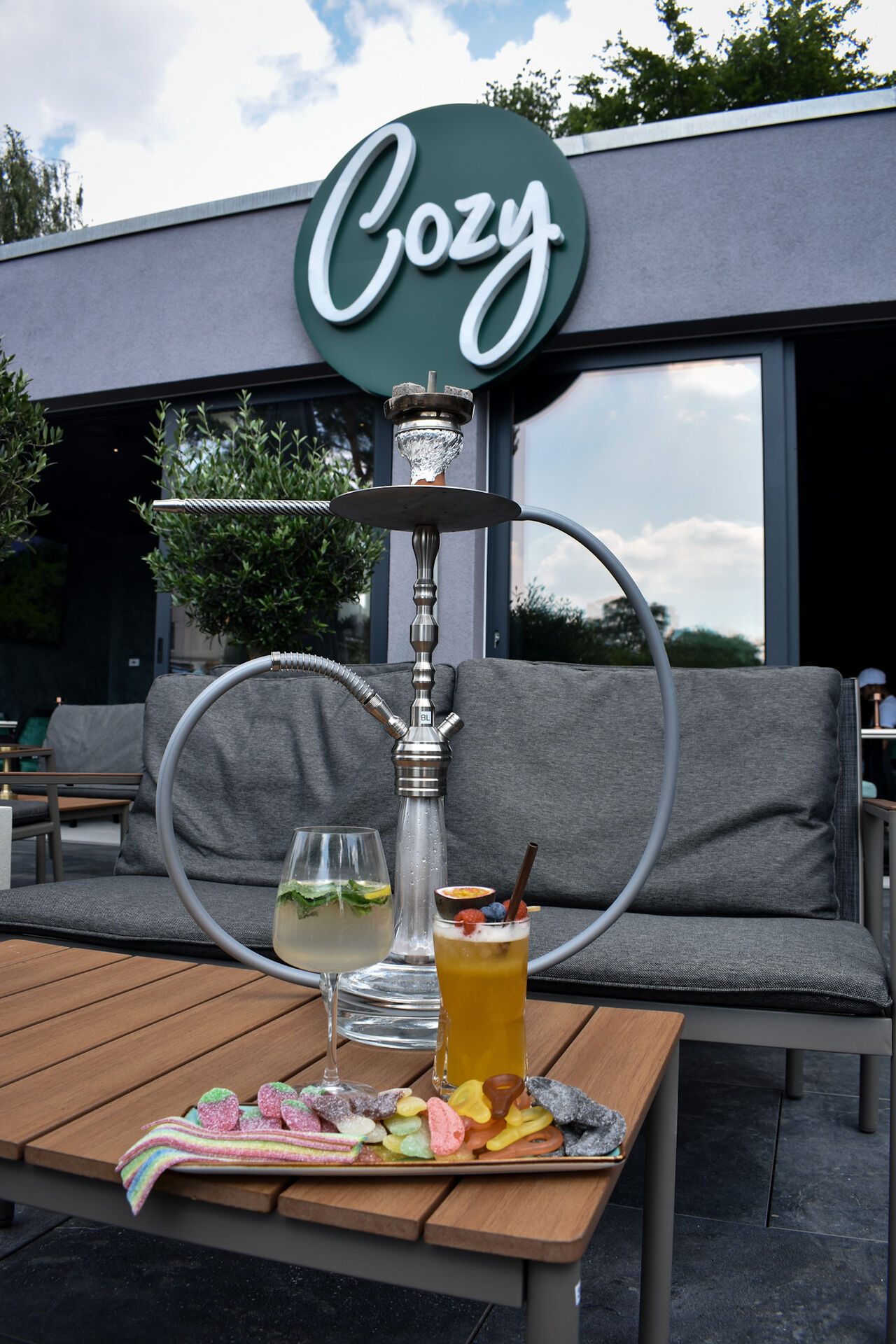 Das runde Cozy-Schild über der Terrasse, davor Shisha und Mocktails