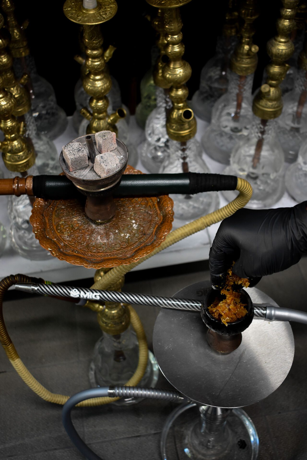 Shisha-Kopf wird mit Naturkohle gebaut, im Hintergrund Wasserpfeifen mit Messing